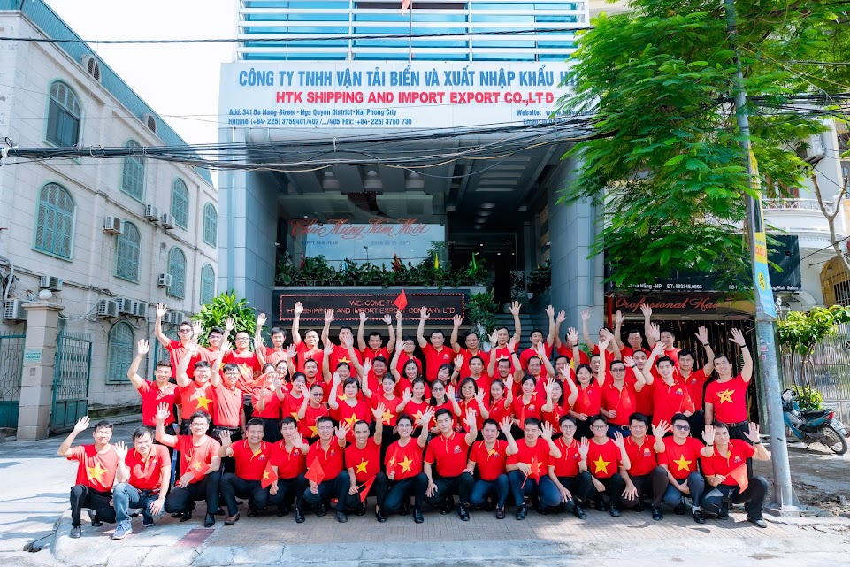 Tập thể HTK chụp ảnh kỉ niệm trước tòa nhà của công ty trongs ắc đỏ rực rỡ